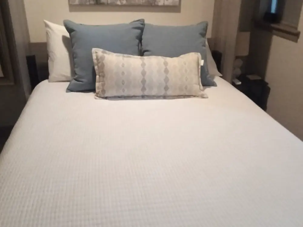 Bed made with fresh white linens and blue pillows