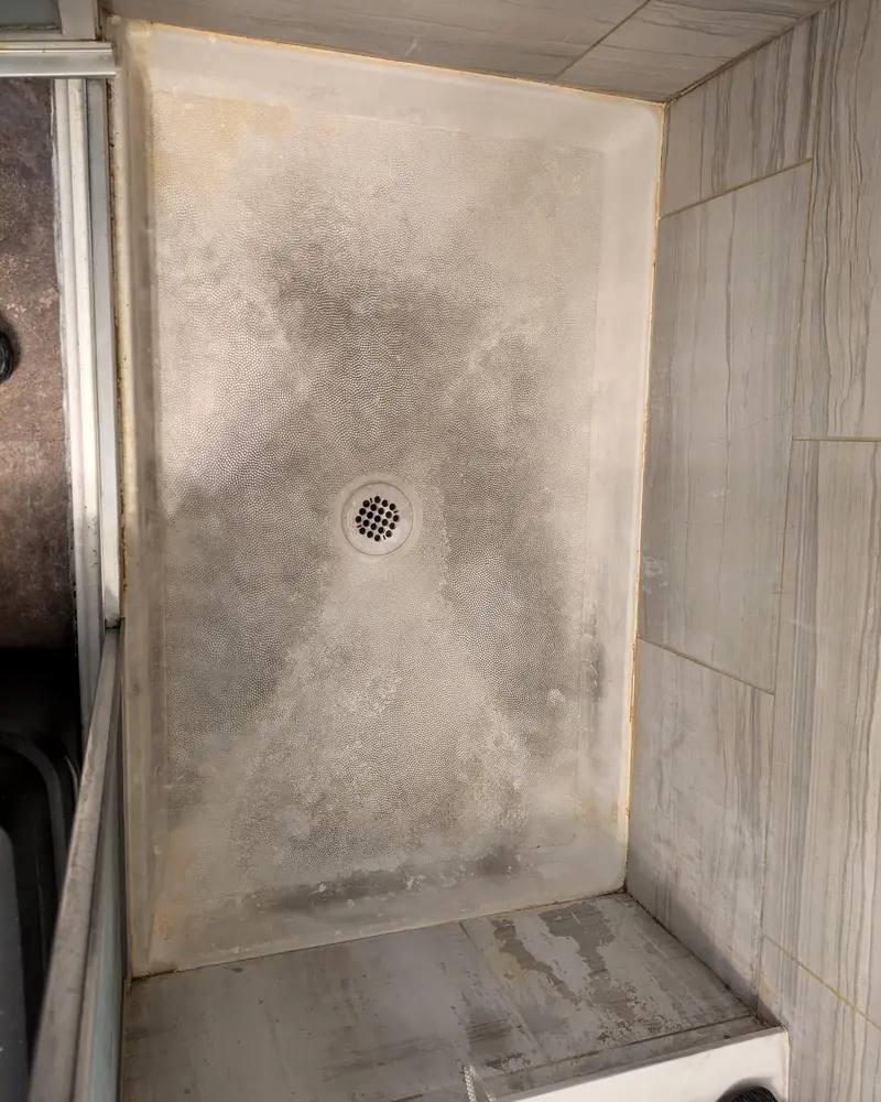 Shower pan stained grey with soap scum and hard water before cleaning